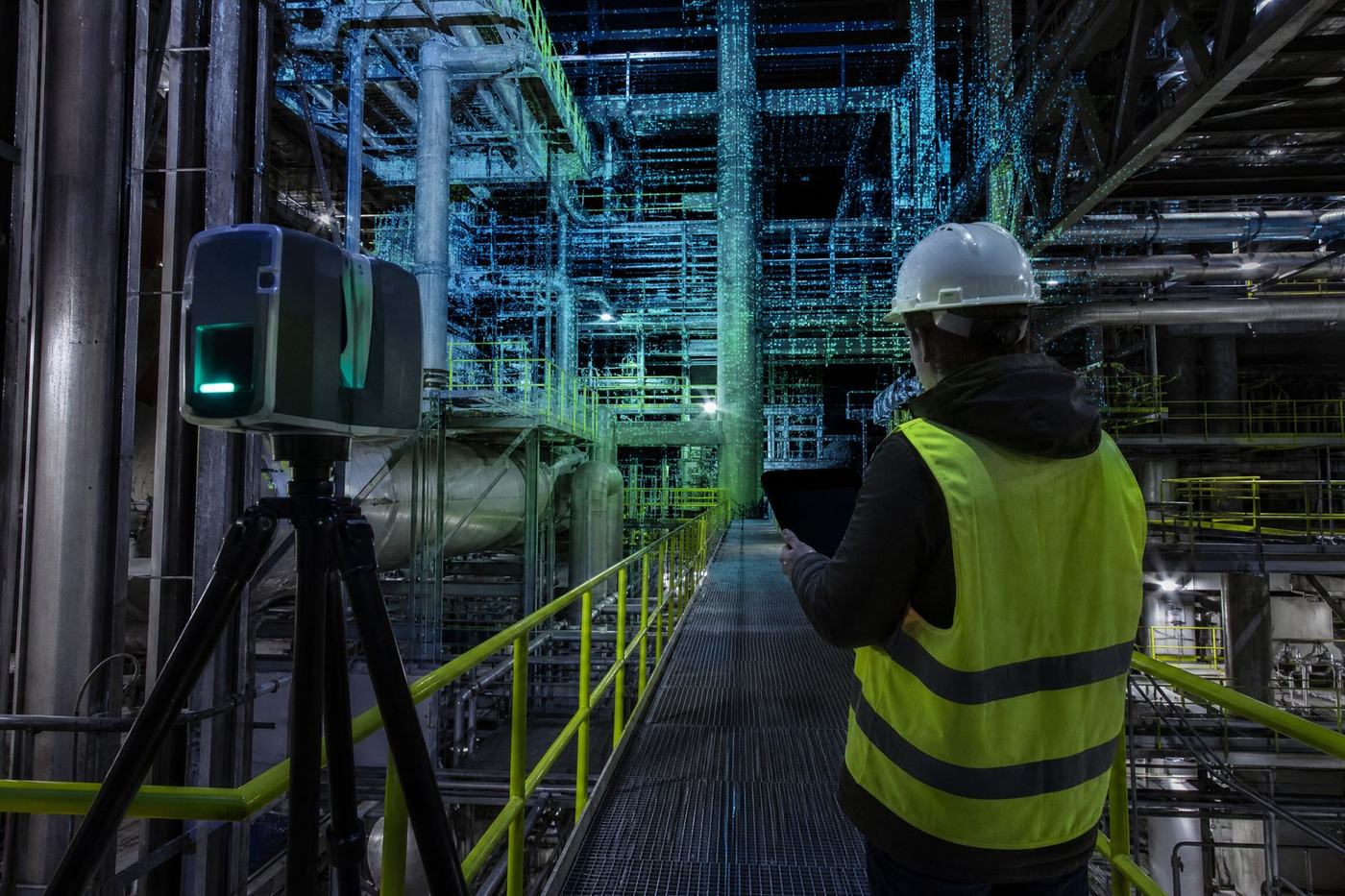 Survey technician in a hard hat and hi-vis vest reviewing scan data on a tablet beside a tripod-mounted laser scanner, on a catwalk in a process plant where the pipework resolves into a cyan point cloud